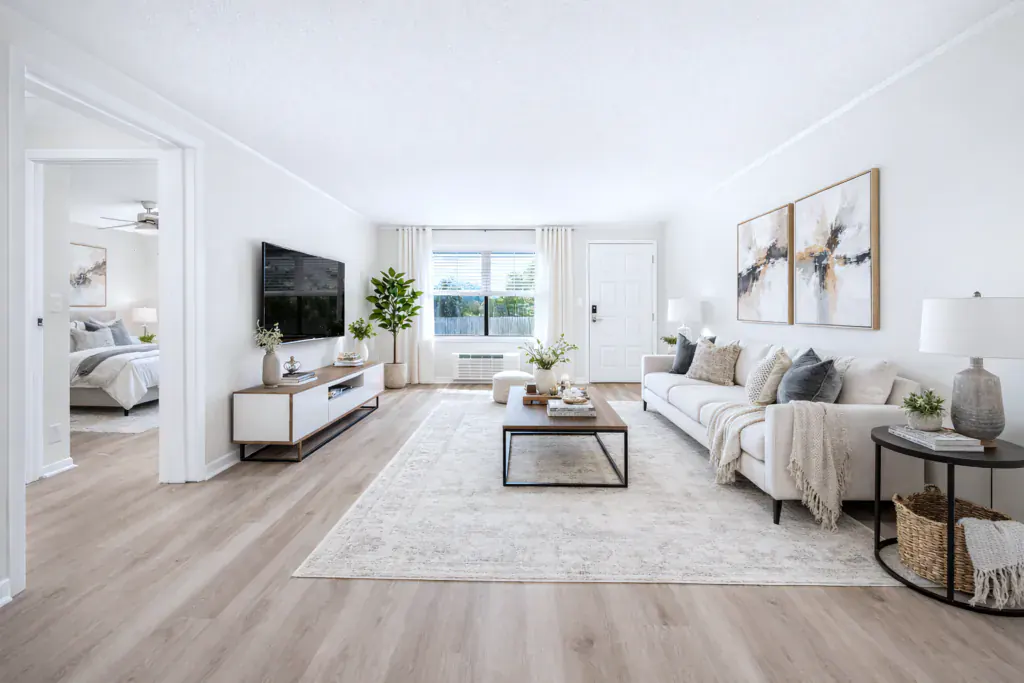 Furnished living room with a sofa, mounted television and rug, opening through a wide doorway to a bedroom beyond