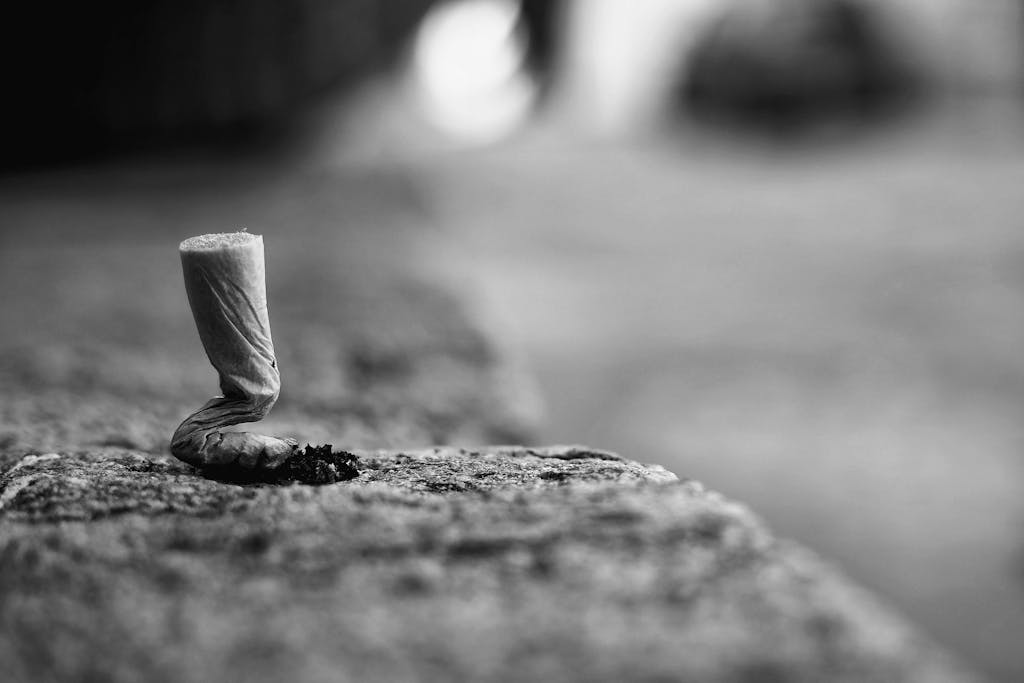 Black and white close-up of a discarded cigarette butt on stone pavement, symbolizing pollution.