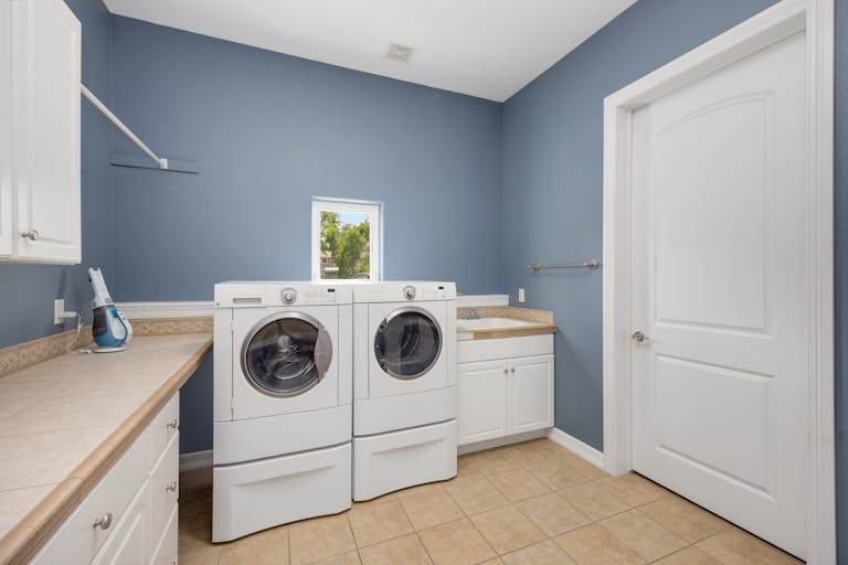 Clean and spacious laundry room featuring modern washing appliances and storage cabinets.